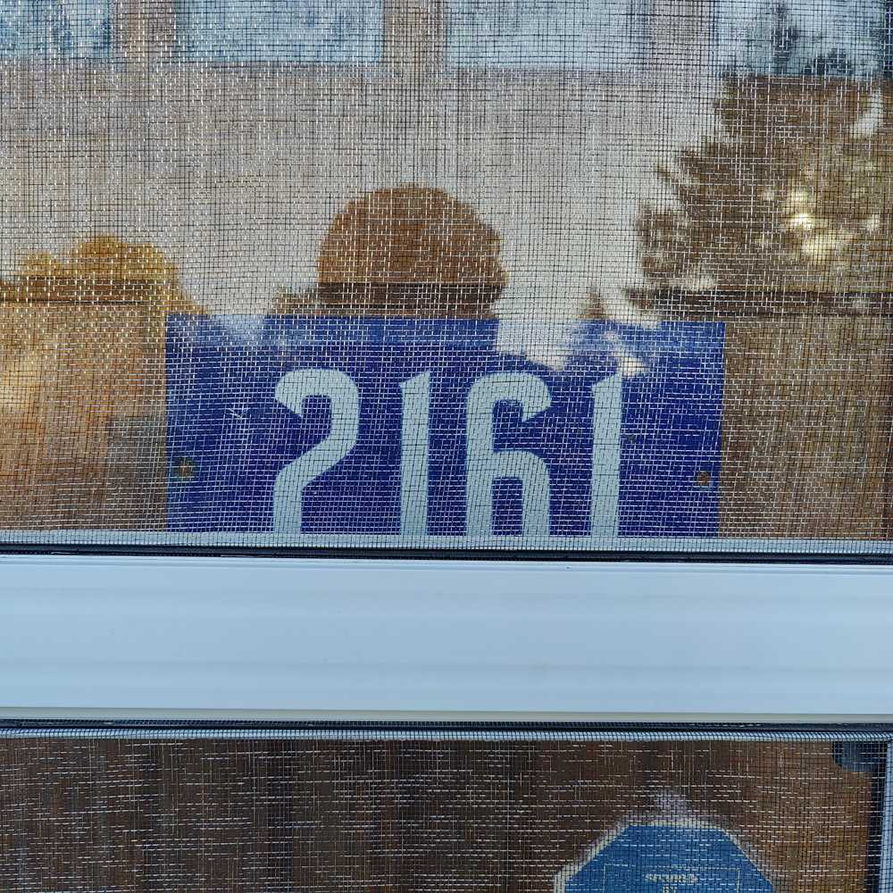 A number plate behind a front door's window screen.